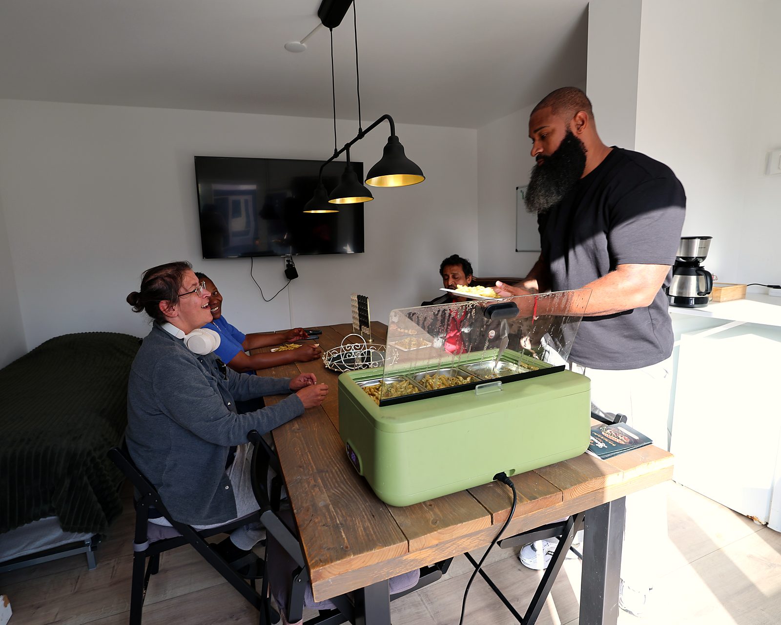 Begeleider en cli&euml;nten eten samen in de woonkamer van GG-Zorg